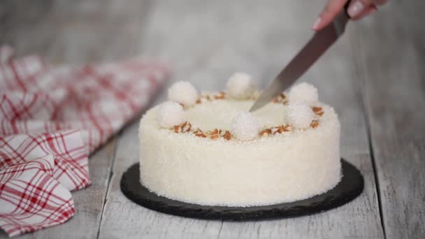 Découper un délicieux gâteau en mousse de noix de coco, décoré de bonbons et d'amandes. — Video