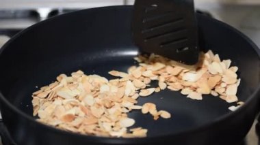 Metal bir tavada, tavada kızartılmış badem fıstığı karıştıran kadın eli..
