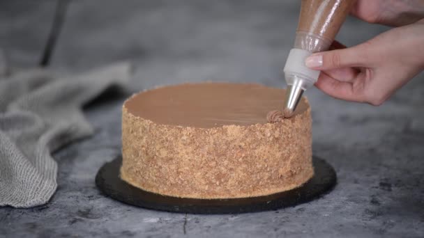 As mãos femininas decoram um bolo com a nata de chocolate de um saco de massa com um bocal. — Vídeo de Stock
