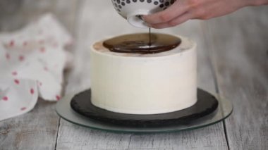 Bir pasta şefinin beyaz kremalı kekin üzerine sıvı çikolata dökerken yakın plan fotoğrafı..