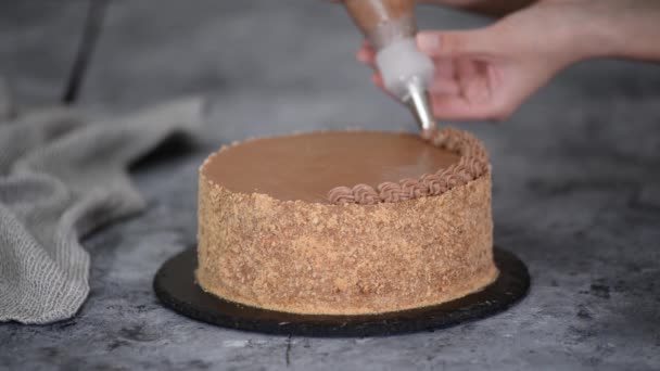 Las manos femeninas decoran un pastel con crema de chocolate de una bolsa de pastelería con una boquilla. — Vídeo de stock