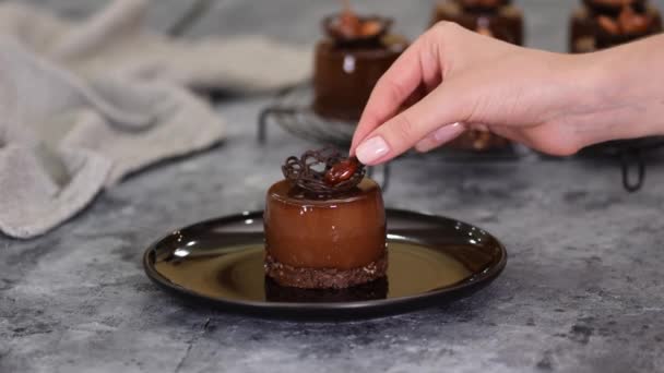 De banketbakker versiert een chocolademousse dessert met karamel amandel. Moderne Europese taart. — Stockvideo
