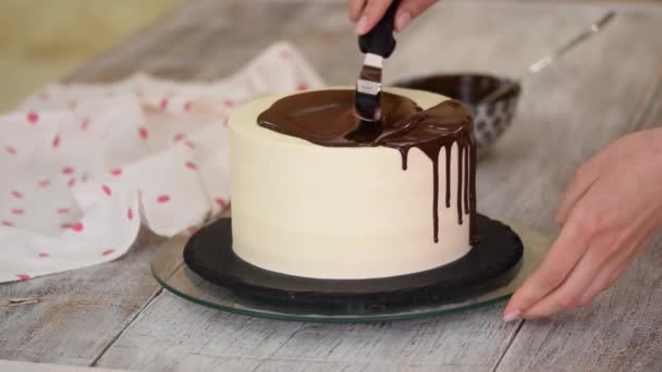 Primer plano de un chef de pastelería vertiendo chocolate líquido en un pastel de crema blanca. — Vídeo de stock