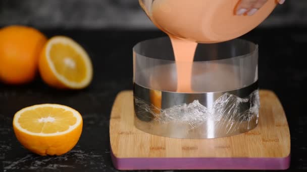 Женщина-кондитер наливает апельсиновый мусс в кондитерское кольцо. Делать торт из мусса на кухне. — стоковое видео