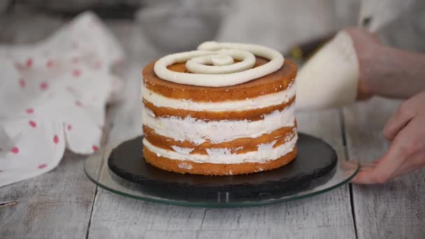 Confeiteiro gira o bolo em um carrinho e decora com creme do saco de pastelaria. — Vídeo de Stock