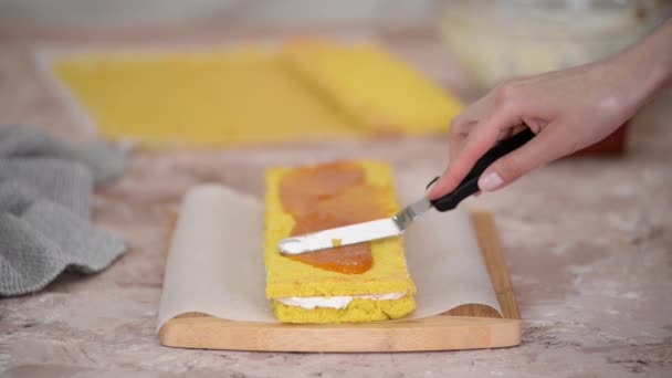 Close-up van de vrouw handen het maken van zoete spons taart met witte room en abrikoos jam. — Stockvideo