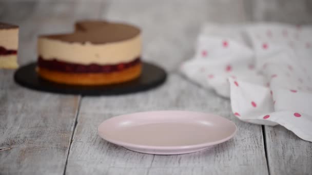 女性パン屋さんがピンクのプレートにキャラメルムースとチェリーケーキの一部を入れています. — ストック動画