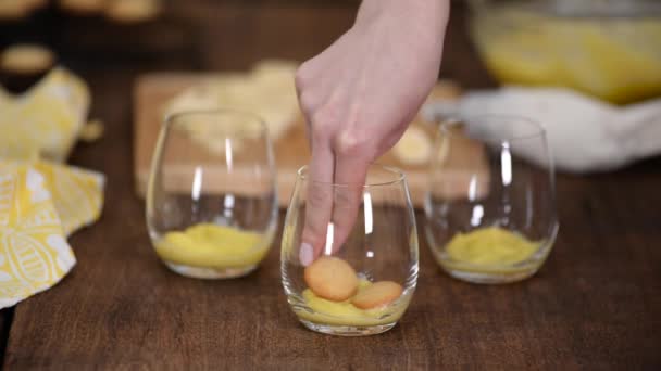 Het meisje dat bananenpudding maakt in glazen glazen glazen in de keuken. Banaan dessert in een glas. — Stockvideo