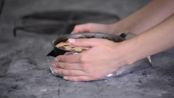 Mutfakta çilek soslu cheesecake hazırlayan kadın. İlkbahar tavasının etrafına alüminyum folyo sarılıyor. — Stok video