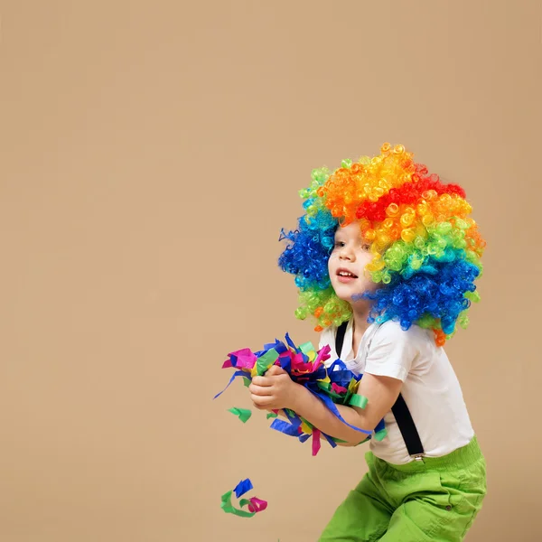 Ευτυχισμένο αγόρι κλόουν με μεγάλη πολύχρωμη περούκα. — Φωτογραφία Αρχείου