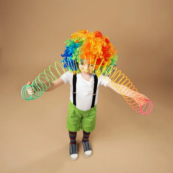 Menino de peruca de palhaço brincando com uma primavera — Fotografia de Stock