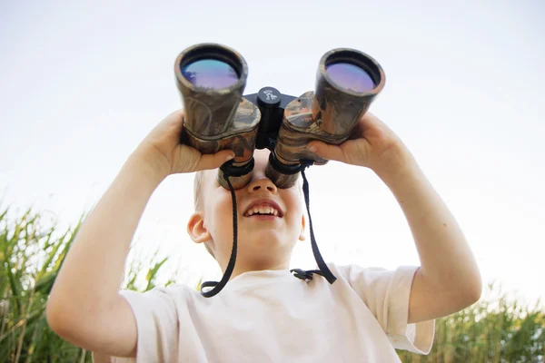 Kleine jongen op zoek door middel van verrekijkers op de rivier bank — Stockfoto