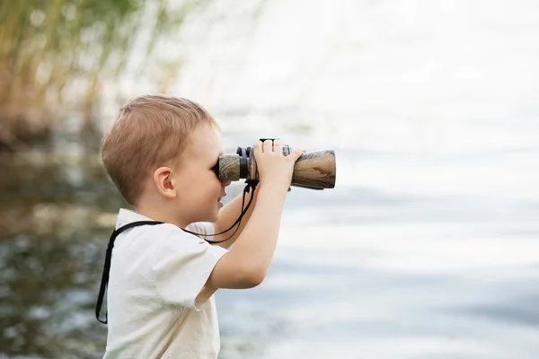 Kleiner Junge blickt durch Fernglas auf Flussufer — Stockfoto