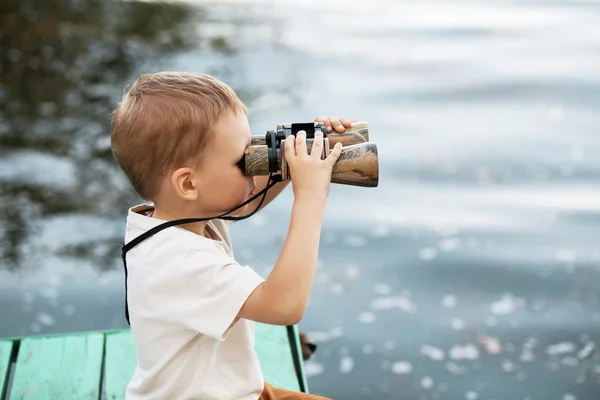 Menino olhando através de binóculos na margem do rio — Fotografia de Stock