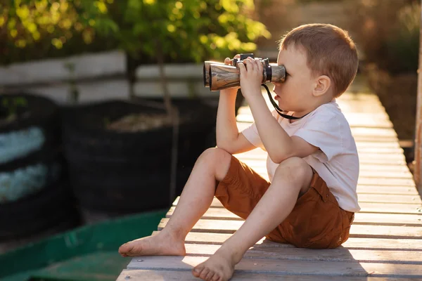 Little boy looking through binoculars on river bank