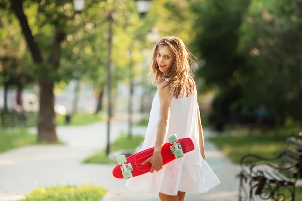 Portrait de belle fille urbaine en robe blanche avec un skatebo rose — Photo