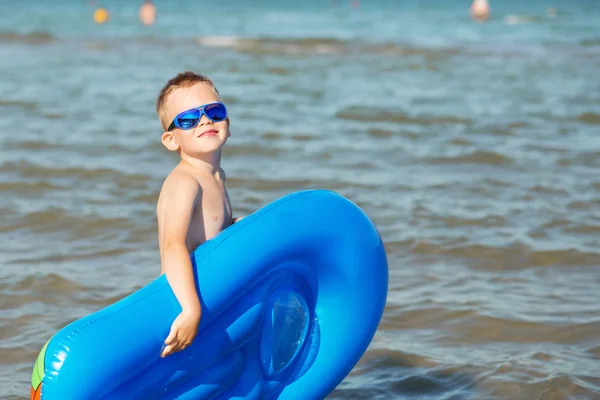 Pequeño niño sosteniendo un colchón inflable en la playa en su caliente — Foto de Stock