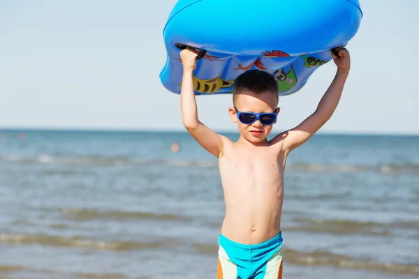 Маленький ребенок держит надувной матрас на пляже на горячий су — стоковое фото