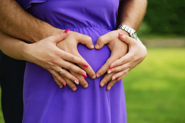 Manos en forma de corazón de la mujer embarazada y su marido — Foto de Stock