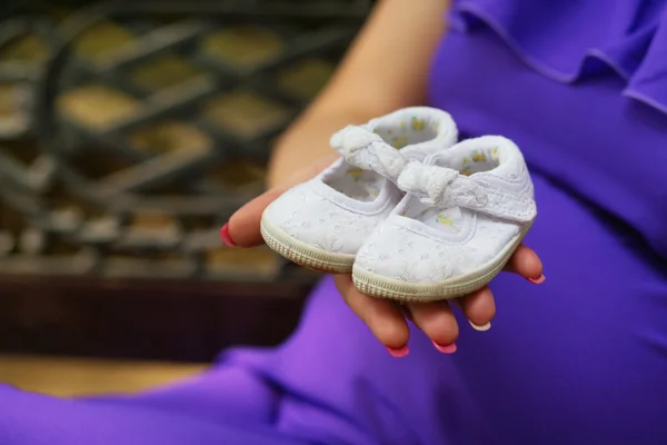 Mulher grávida segurando sapatos de bebê em sua mão — Fotografia de Stock