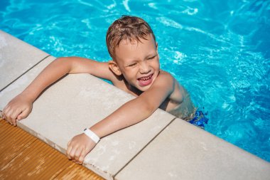 Happy kid playing in blue water of swimming pool. clipart