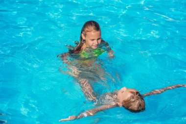 Happy kids playing in blue water of swimming pool. clipart