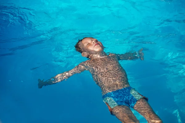 Szczęśliwe dziecko grając w niebieski wody z basenu. — Zdjęcie stockowe