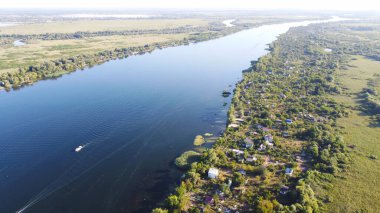 İnsansız hava aracı, çeşitli binaları ve bataklık habitatı olan ve Common Reed hava manzaralı yerel köyle çevrili bir nehrin üzerinde uçuyor. Üst görünüm.