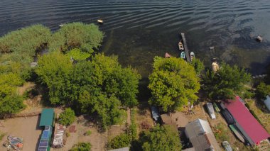 İnsansız hava aracı, çeşitli binaları ve bataklık habitatı olan ve Common Reed hava manzaralı yerel köyle çevrili bir nehrin üzerinde uçuyor. Üst görünüm.