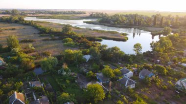 İnsansız hava aracı, çeşitli binaları ve bataklık habitatı olan ve Common Reed hava manzaralı yerel köyle çevrili bir nehrin üzerinde uçuyor. Üst görünüm.