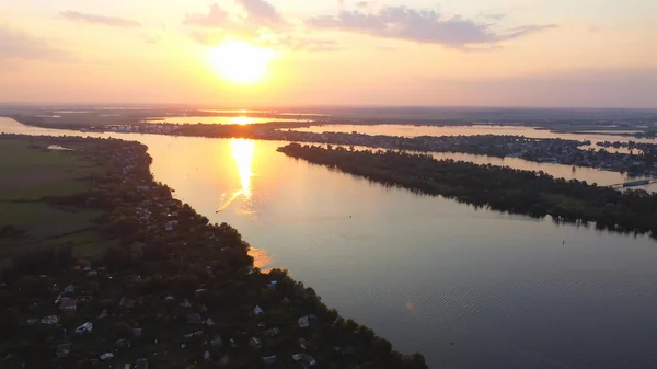 Drone fly over waving river surrounded by local village with various buildings and Wetland and marsh habitat with a reedbed of Common Reed aerial view at Sunset. Top view.