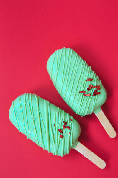 cake - popsicle in green glaze on a red background. space for text. Ice cream sweet eskimo with chocolate icing.  Chocolate covered ice cream on stick. Cake sweets desserts 