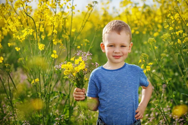 Rapaz bonito com um buquê de flores está na ra floração amarela — Fotografia de Stock