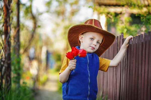 Πορτρέτο ενός μικρού αγοριού που στέκεται σε ένα μεγάλο καπέλο με ένα μπουκέτο από — Φωτογραφία Αρχείου