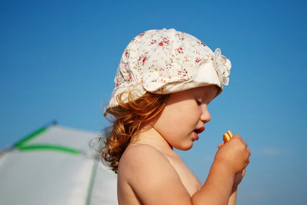 Meisje bedekt met kruimels eet cookies op het strand — Stockfoto