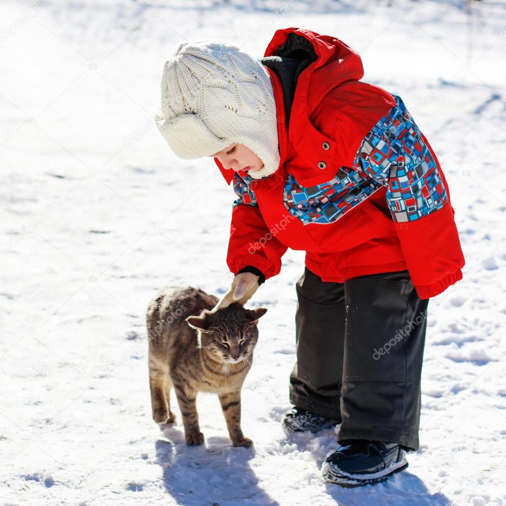 Little boy playing with cat outdoors in winter