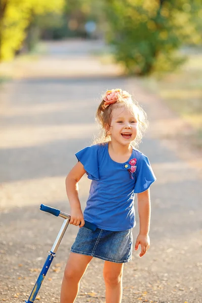 Portrait of playful fun smiling little girl with scooter in the — Stock Photo, Image