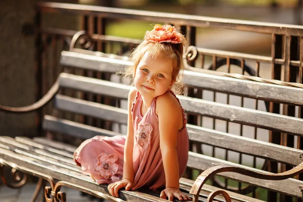 Porträtt av en leende liten flicka sitter på en parkbänk — Stockfoto