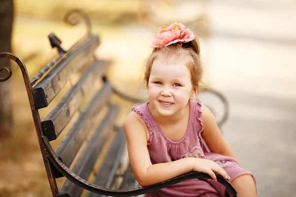Retrato de uma menina bonita sorridente sentada em um banco de parque — Fotografia de Stock