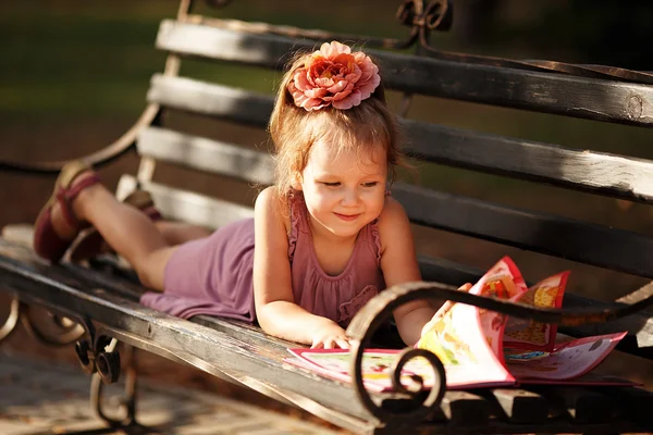 Porträt eines kleinen Mädchens, das ein Kinderbuch liest, das auf einem Blatt liegt — Stockfoto