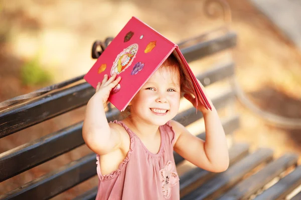 Retrato de una niña riendo con un libro en la cabeza — Foto de Stock