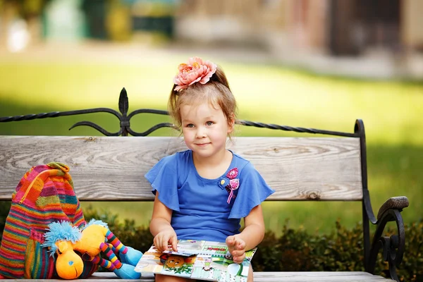 Portrait of a little girl reading a children's book on a park be — Stock Photo, Image