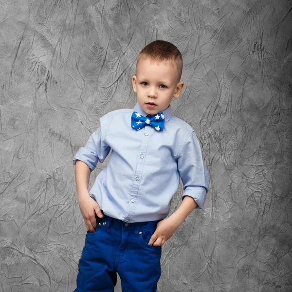 Retrato de um menino bonito em jeans, camisa azul e laço — Fotografia de Stock