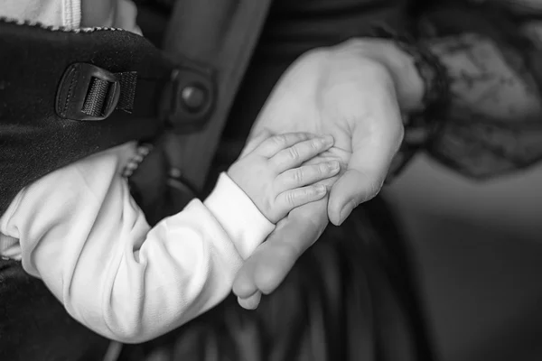 Mamá sostiene al bebé de la mano durmiendo en un portabebés ergonómico — Foto de Stock