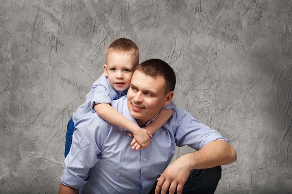 Vader en zoontje in blauwe shirts voor grijze achtergrond — Stockfoto