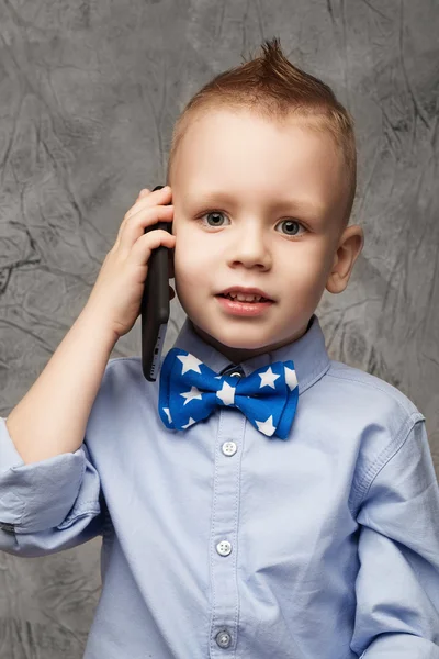 Portret van kleine jongen in het blauwe shirt en strikje met mobiele pho — Stockfoto