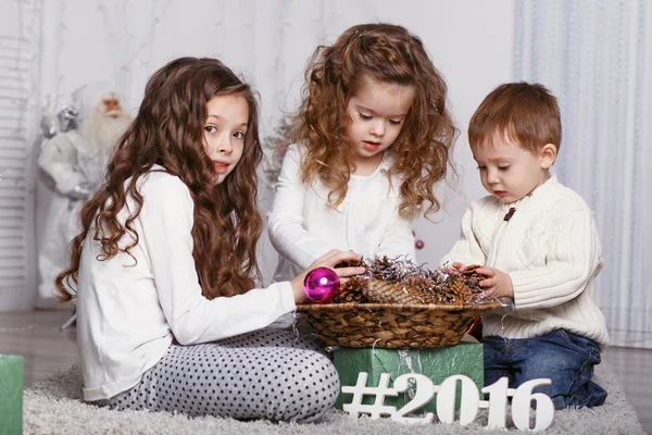 Três irmãos pequenos que decoram a árvore de Natal com o abeto-cone . — Fotografia de Stock