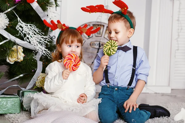 Menina e menino em chifres de rena comendo um pirulitos . — Fotografia de Stock