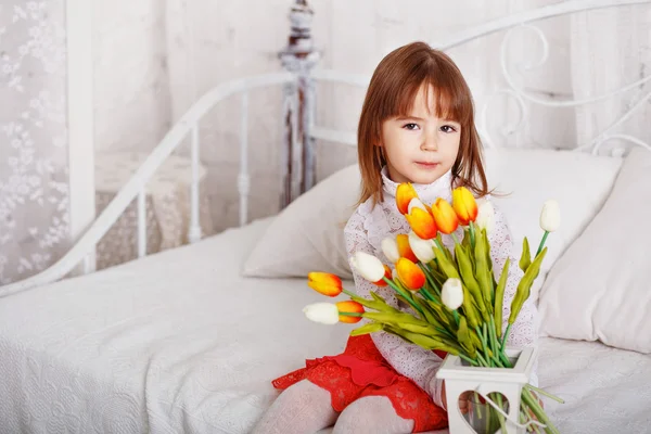 Красива маленька дівчинка сидить на ліжку з букетом білого і — стокове фото