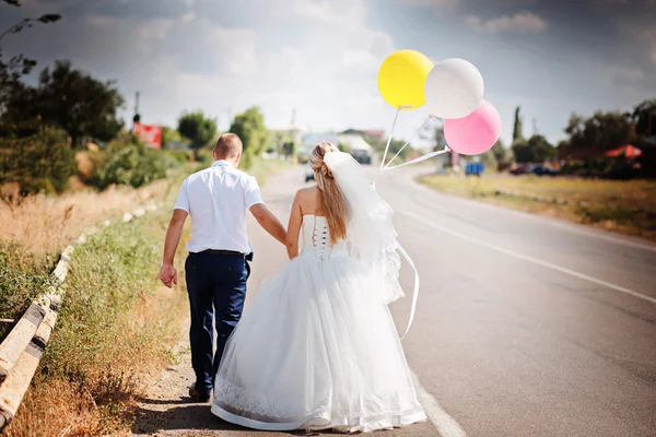 Heureux couple marié avec des ballons marcher ensemble sur la route — Photo